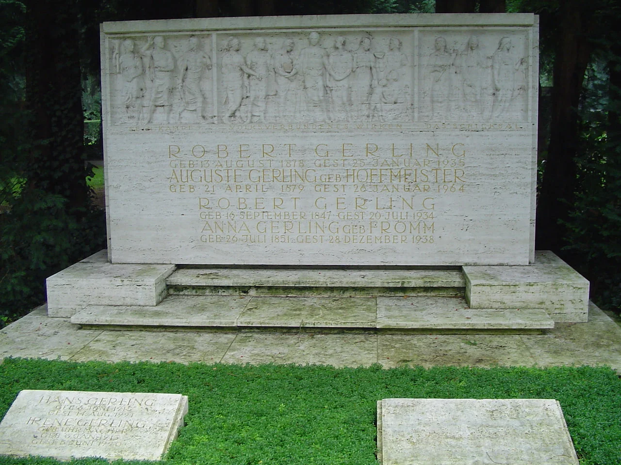 Monumentale helle Familiengrabstätte Gerling mit langem Figurenrelief, eingemeißelten Namen und zwei flachen Grabplatten im Vordergrund auf Nordfriedhof Köln